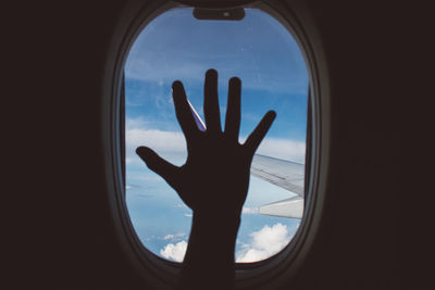 Silhouette of person hand against sky seen through window