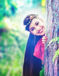 Portrait of smiling woman standing behind tree trunk