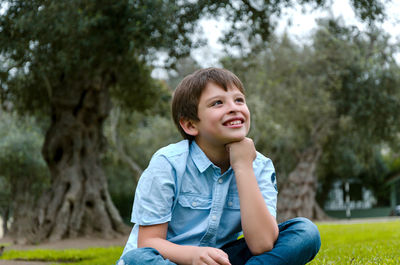 Portrait of boy sitting on land against trees