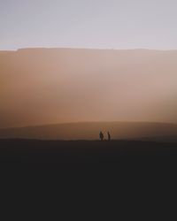 Silhouette people on land against sky during sunset