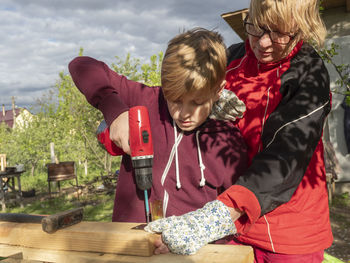 Grandmother with grandson drilling wood on table