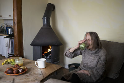 Senior woman sitting next to fireplace and drinking from glass