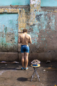 Rear view of shirtless man standing against wall