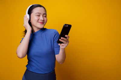 Mid adult man using mobile phone against yellow background