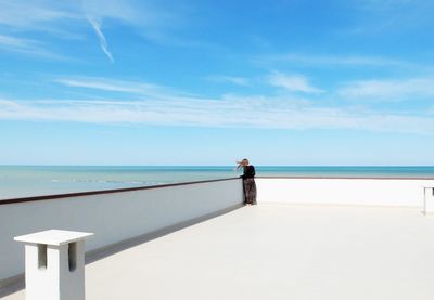 Rear view of woman standing by retaining wall over sea against sky