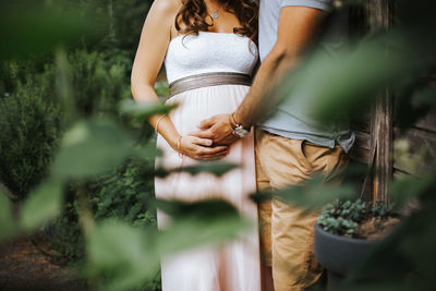 Midsection of man holding pregnant wife while standing by plants