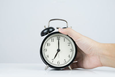 Close-up of hand holding clock against white background