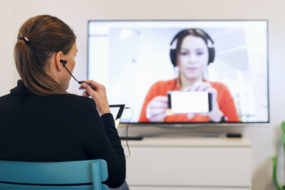 Rear view of businesswoman using in-ear headphones during conference call in creative office