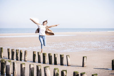 Man jumping at beach against sky