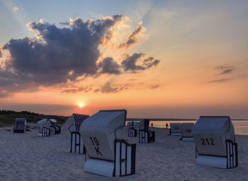 Hooded chairs on beach against sky during sunset