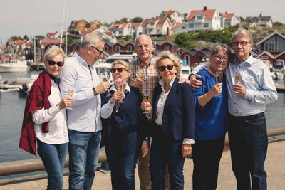 Happy senior male and female friends enjoying champagne on pier during vacation
