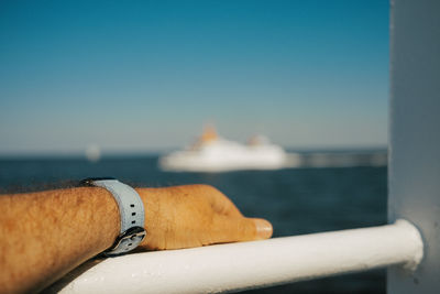 Low section of person on ferry in sea with light blue watchband on wrist