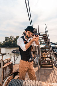 Full length of young man holding camera against sky