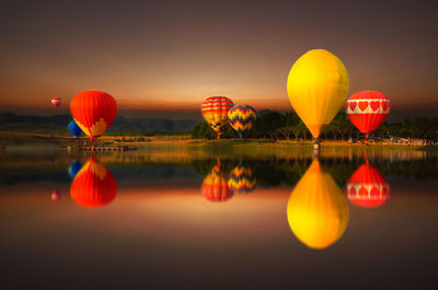 Colorful hot air balloons flying over the lake with reflection on the water at golden hour twilight.