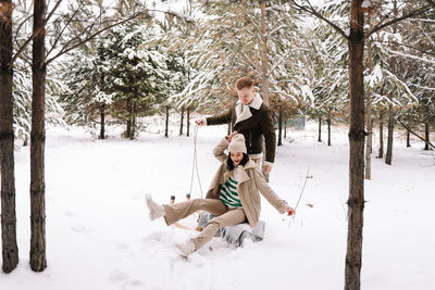 A man and a woman in love have fun and ride a sleigh in forest among the trees in winter in nature