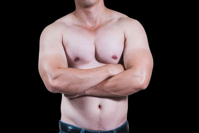 Midsection of shirtless man standing with arms crossed against black background