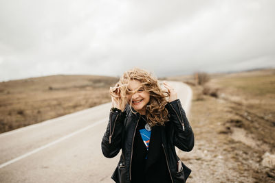 Portrait of young woman standing on road against sky