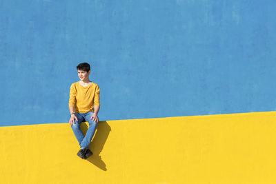 Full length of boy sitting against wall