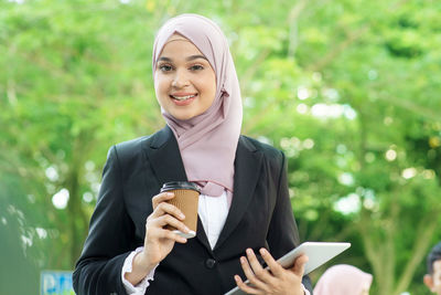 Portrait of smiling businesswoman holding digital tablet and disposable cup