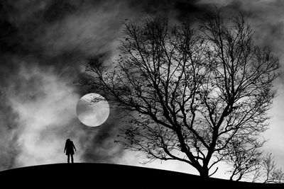 Rear view of silhouette man standing on field by bare trees against full moon at night