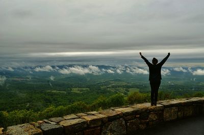 Man standing on landscape against cloudy sky