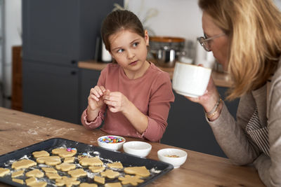 Grandmother drinking coffee while granddaughter making cookies
