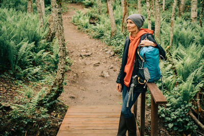 A woman in a raincoat and a hat in the thickets of the forest enjoys the freshness after the rain