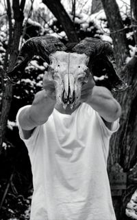 Man holding animal skull while standing against trees