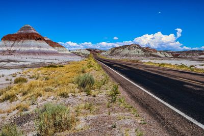 Road leading towards mountains against blue sky