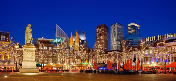 Illuminated buildings against blue sky at night