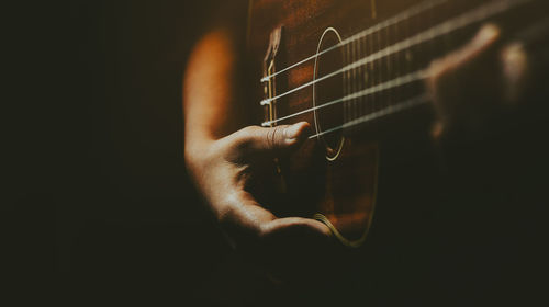 Close-up of hand playing guitar against black background