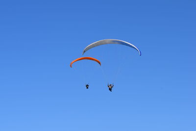 Low angle view of person paragliding against clear blue sky