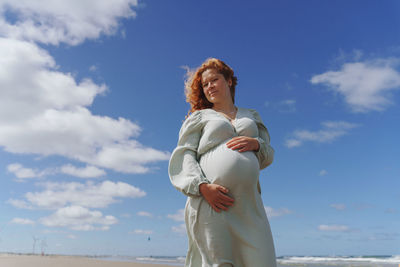 Rear view of pregnant woman standing at beach against sky