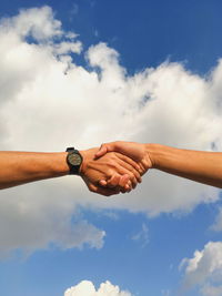 Close-up of couple holding hands against sky