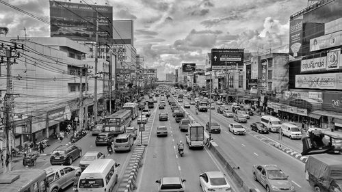 Vehicles moving on city street amidst buildings against cloudy sky