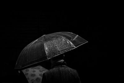 Rear view of man holding umbrella against black background