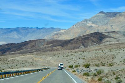 Vehicles on road by mountain against sky