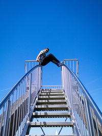 Low angle view of man on steps against clear blue sky