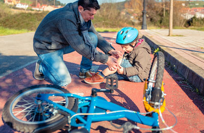 Father applying bandage on fallen son wound by bicycle on road