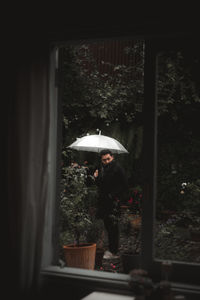 Man holding umbrella seen through window