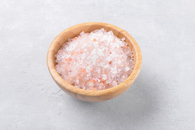 Pink himalayan salt in a wooden bowl on a light grey background, close up