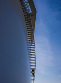 Low angle view of worker moving up steps of storage tank at oil refinery