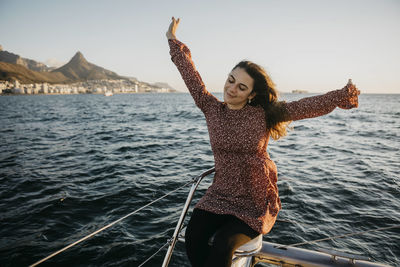 Young woman with arms raised sitting on boat in sea at weekend