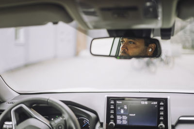 Reflection of male commuter on rear-view mirror in car