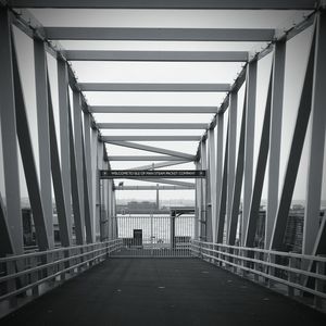 Elevated walkway leading towards suspension bridge against sky