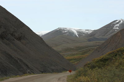 Country road leading towards mountains against sky