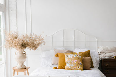Bedroom interior, white bed with pillows and autumn decor, dried flowers in a vase