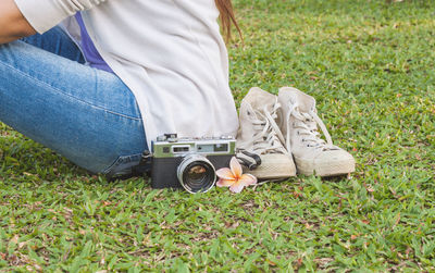 Midsection of woman sitting by vintage camera and sneakers on grassy field