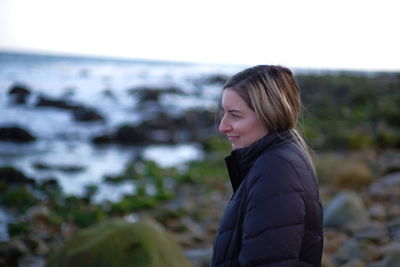 Side view of smiling young woman standing against sea