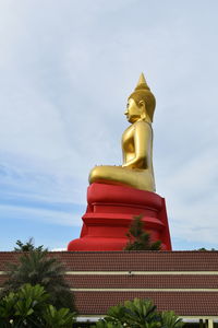 Low angle view of gold buddha statue against sky